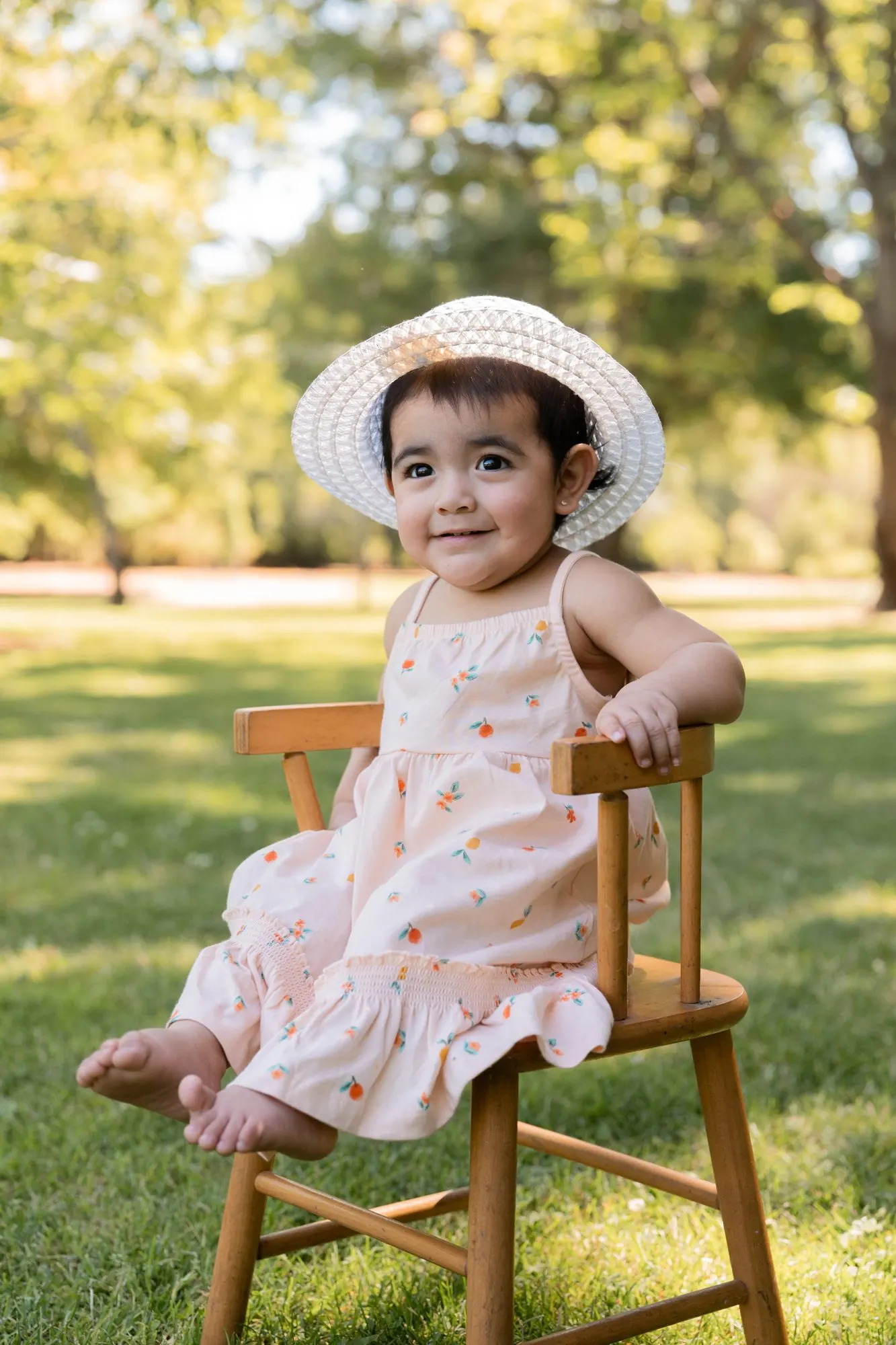 Toddler in a sun hat sitting on a small wooden chair in a park